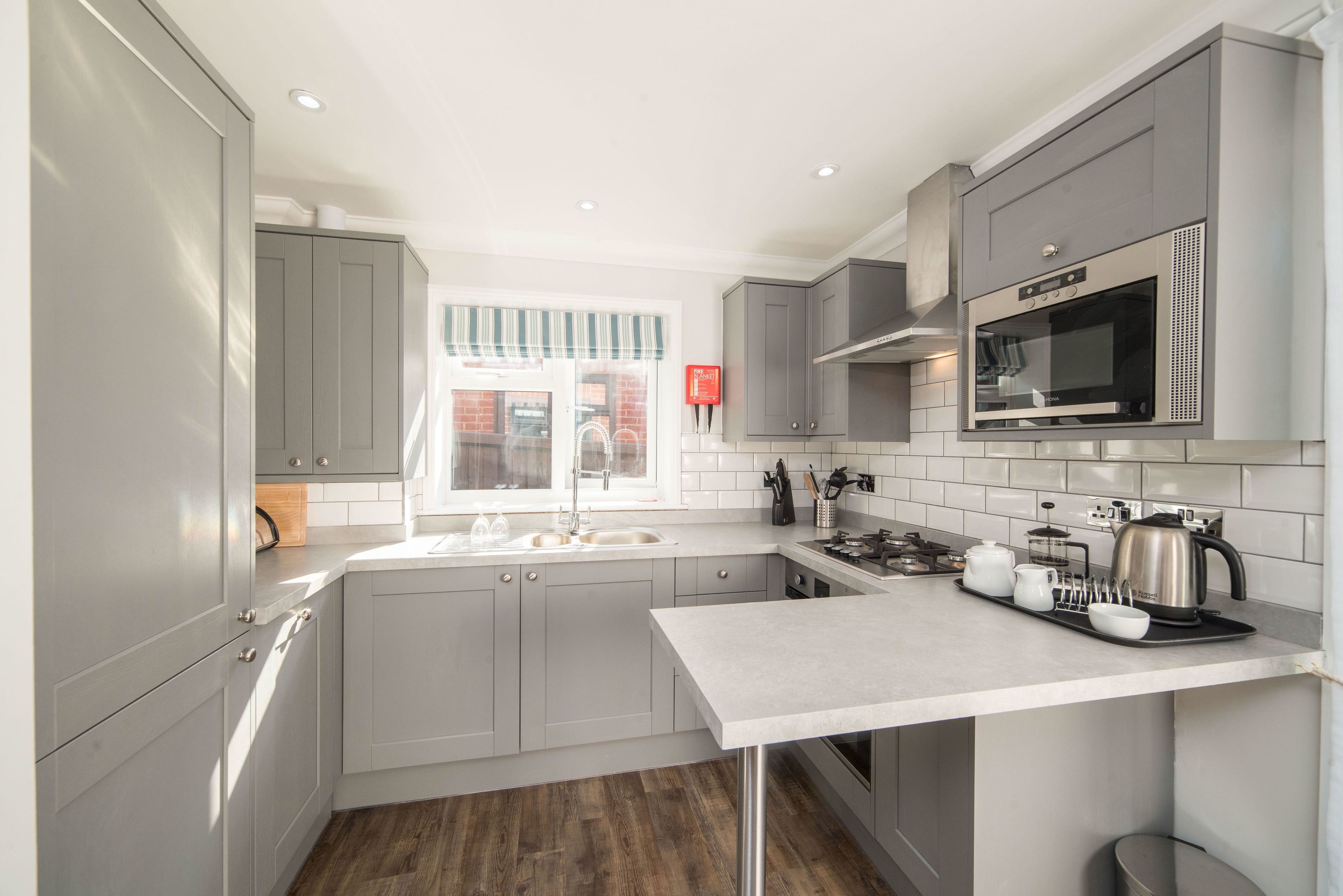 A modern kitchen with grey cabinets, a stainless steel microwave, and a window with a striped valance.