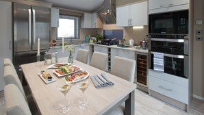 A modern kitchen with a dining table set for a meal, featuring stainless steel appliances, a skylight, and a view of the outdoors. - The Lakes Rookley Holiday Park (Ventnor)