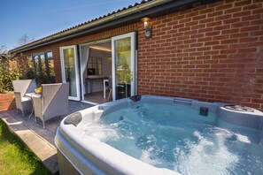 A hot tub in a backyard with a brick wall, sliding glass doors, and outdoor furniture.