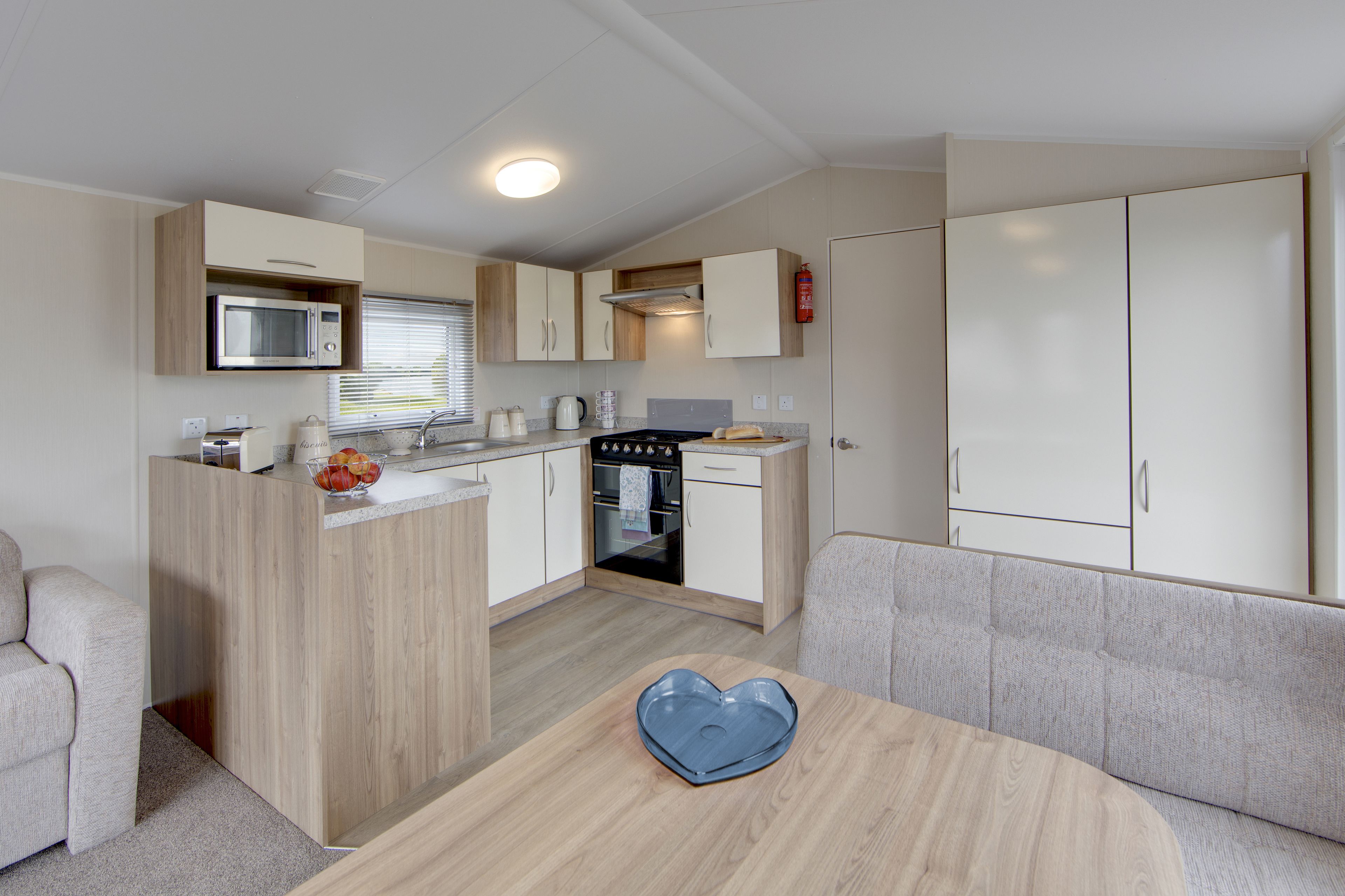 A compact kitchenette with a microwave, oven, and sink. There is a small seating area with a heart-shaped tray on the table.