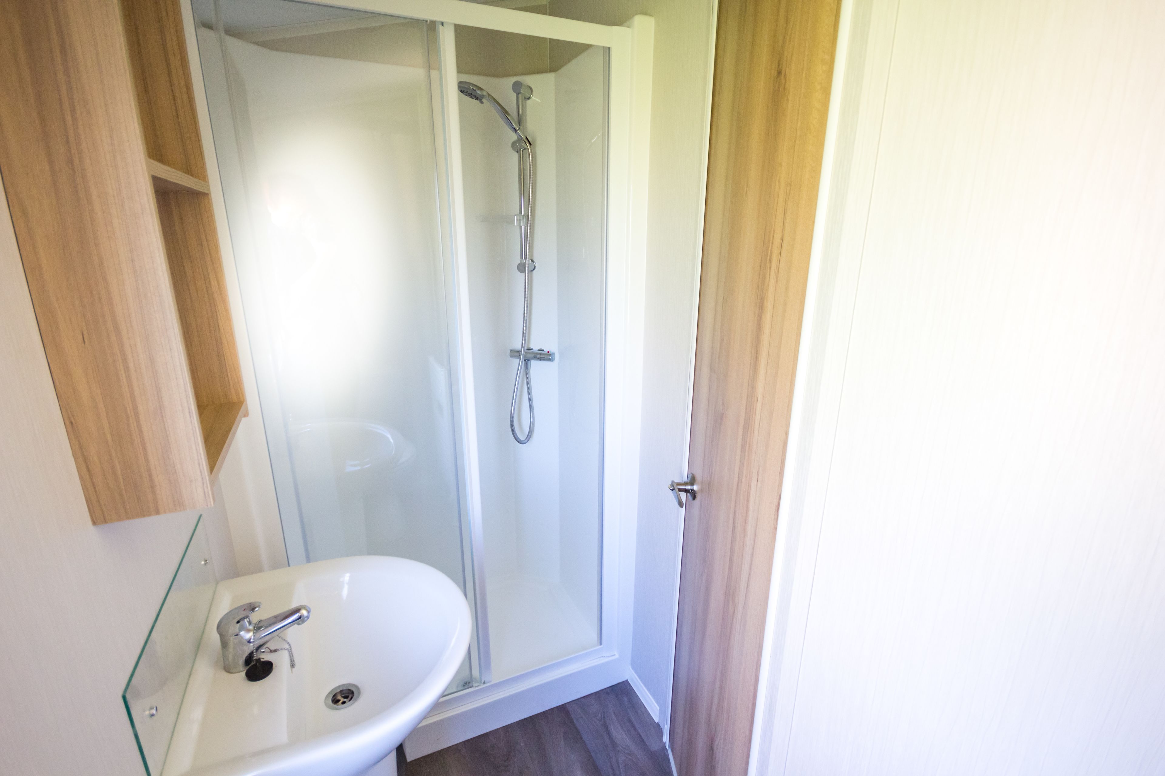 A bathroom with a glass-enclosed shower, a white sink, and a wooden cabinet.