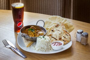 A plate of food with rice, naan bread, and a curry dish, accompanied by a glass of iced tea and condiments.