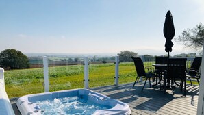 A hot tub on a wooden deck with a view of a green field and distant hills. - The Lakes Rookley Holiday Park (Ventnor)