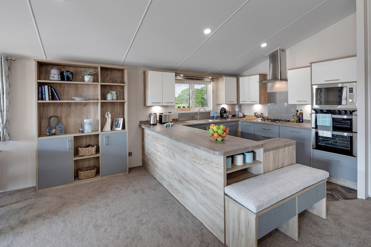 A modern kitchen with a central island, built-in shelves, and a large window.