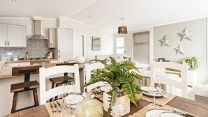 A modern kitchen with white cabinetry, a brick backsplash, and a dining area with a wooden table and chairs. - St Helens Coastal Resort (Ryde)