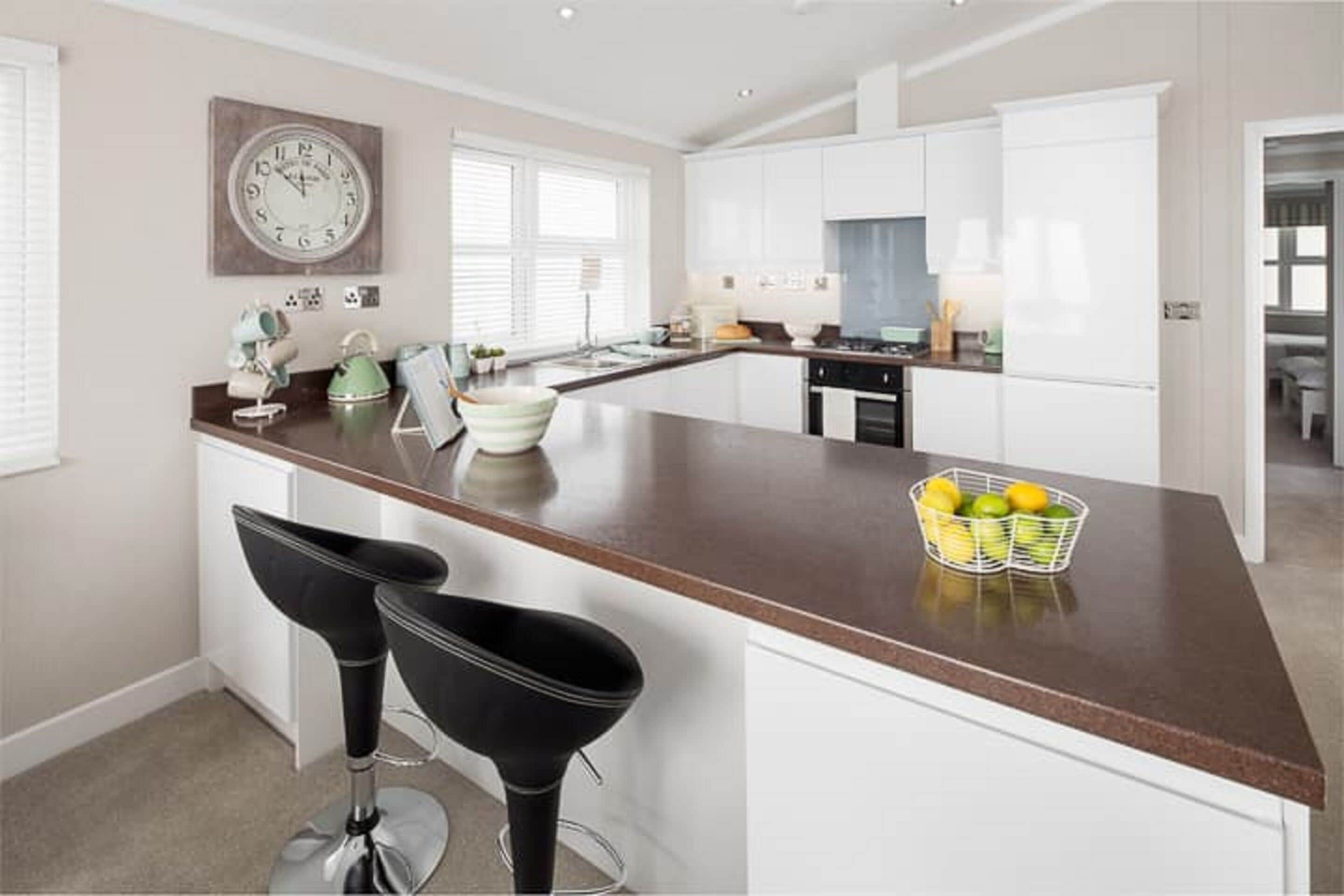 A modern kitchen with white cabinets, a brown countertop, and two black bar stools.