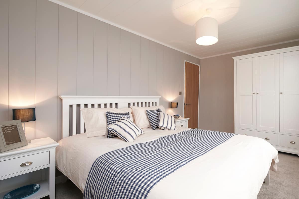 A bedroom with a bed, nightstands, a lamp, a wardrobe, and a framed picture on the nightstand.