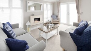 A living room with a fireplace, a coffee table, and two sofas with patterned cushions. - St Helens Coastal Resort (Ryde)