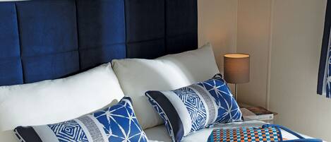 A bed with a blue upholstered headboard, white bedding, and patterned pillows.