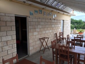 A covered patio area with brick walls, wooden furniture, and a door leading to an interior space. - Hostal Nueva Vida (Ciénaga de Zapata)