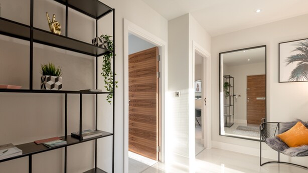 A modern living room with a black metal shelving unit, a wooden door, a large mirror, and a plush chair with an orange cushion. - Silver Lining - Penthouse with parking (Edinburgh)