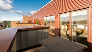 A rooftop terrace with a wooden deck, a glass sliding door leading to a seating area, and a brick wall. - Silver Lining - Penthouse with parking (Edinburgh)