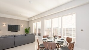 A modern dining area with a round glass table, grey upholstered sofa, and wooden chairs. - Silver Lining - Penthouse with parking (Edinburgh)