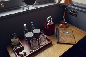 A wooden tray with a red kettle, a lamp, and a tray of mugs and glasses on a table.