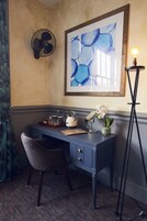 Una scrivania d'angolo con una sedia, un quadro astratto incorniciato, una lampada da terra e una piccola orchidea in vaso.
