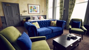 A room with a blue sofa, green armchairs, a bed with colorful pillows, and a window with curtains. - Frederick Street Townhouse (Birmingham)