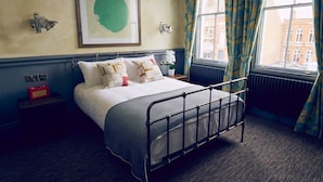 A neatly made bed with a metal frame, a framed artwork on the wall, and a window with curtains. - Frederick Street Townhouse (Birmingham)