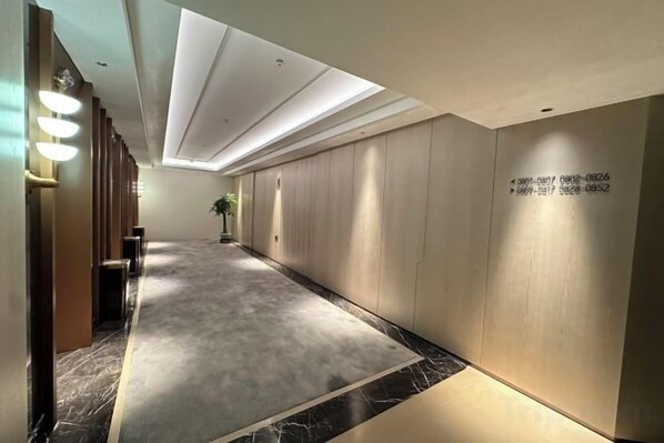 A hotel corridor with a marble floor, wooden paneling on the walls, and recessed lighting.