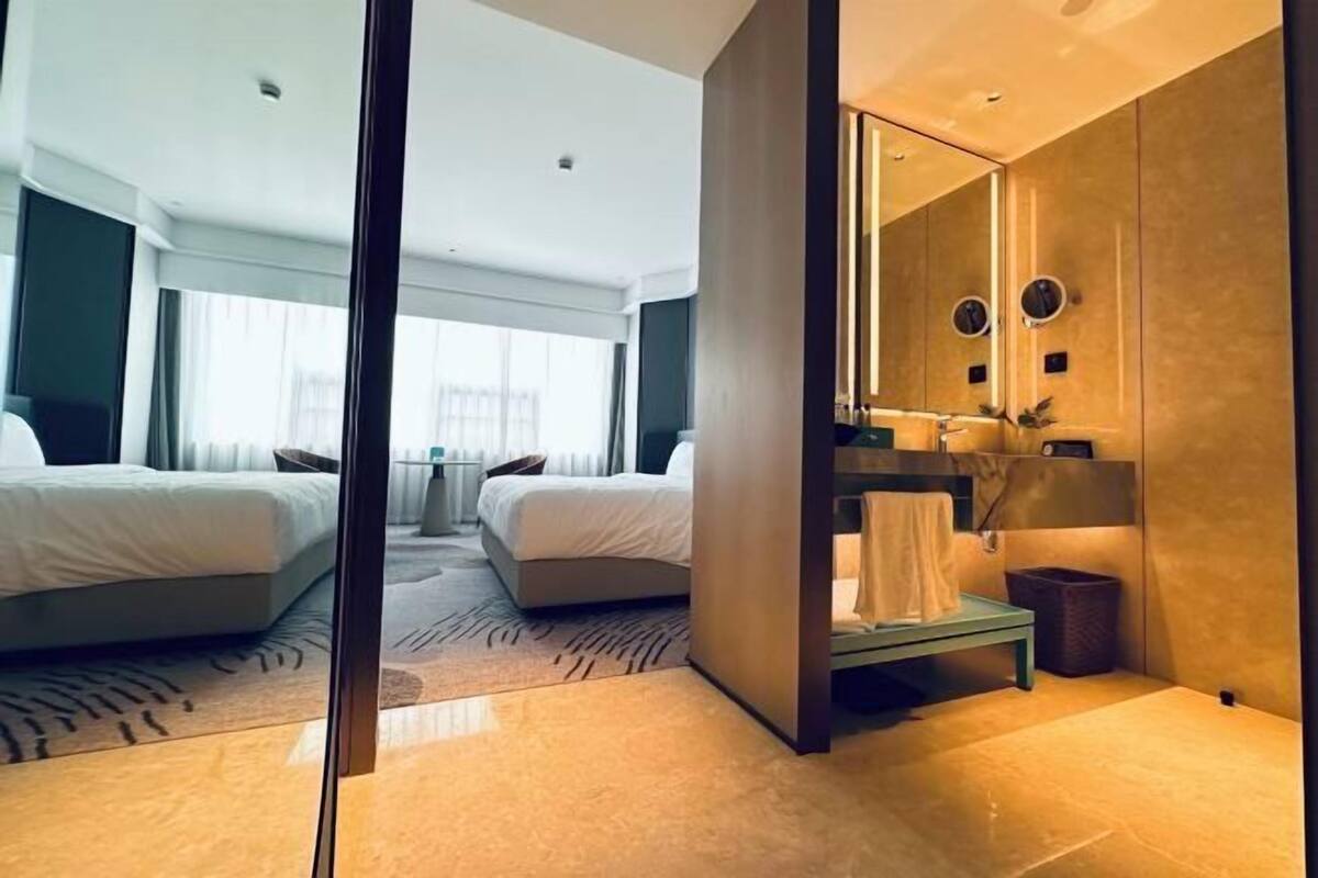 Ein modernes Hotelzimmer mit einem großen Bett, einer separaten Sitzecke, einem Schminktisch mit Spiegel und Blick ins Freie.