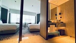 A modern hotel room with a large bed, a separate seating area, a vanity with a mirror, and a view of the outdoors.