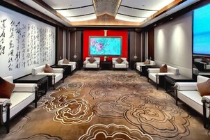 Un salón de conferencias con piso alfombrado, sofás blancos y una pantalla grande al frente.