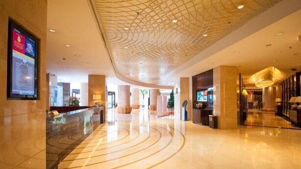 A spacious lobby with a curved floor design, a modern ceiling with a geometric pattern, and a reception area with a digital display.