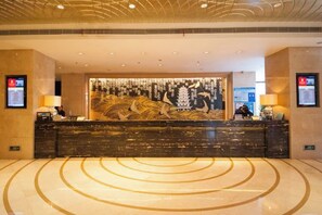 Zona de recepción de un hotel con diseño moderno, que incluye un mostrador grande, una pared decorativa con patrones abstractos y un piso de mármol pulido.