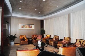 A hotel lobby with a round table, multiple sofas, a potted plant, and a framed artwork on the wall.