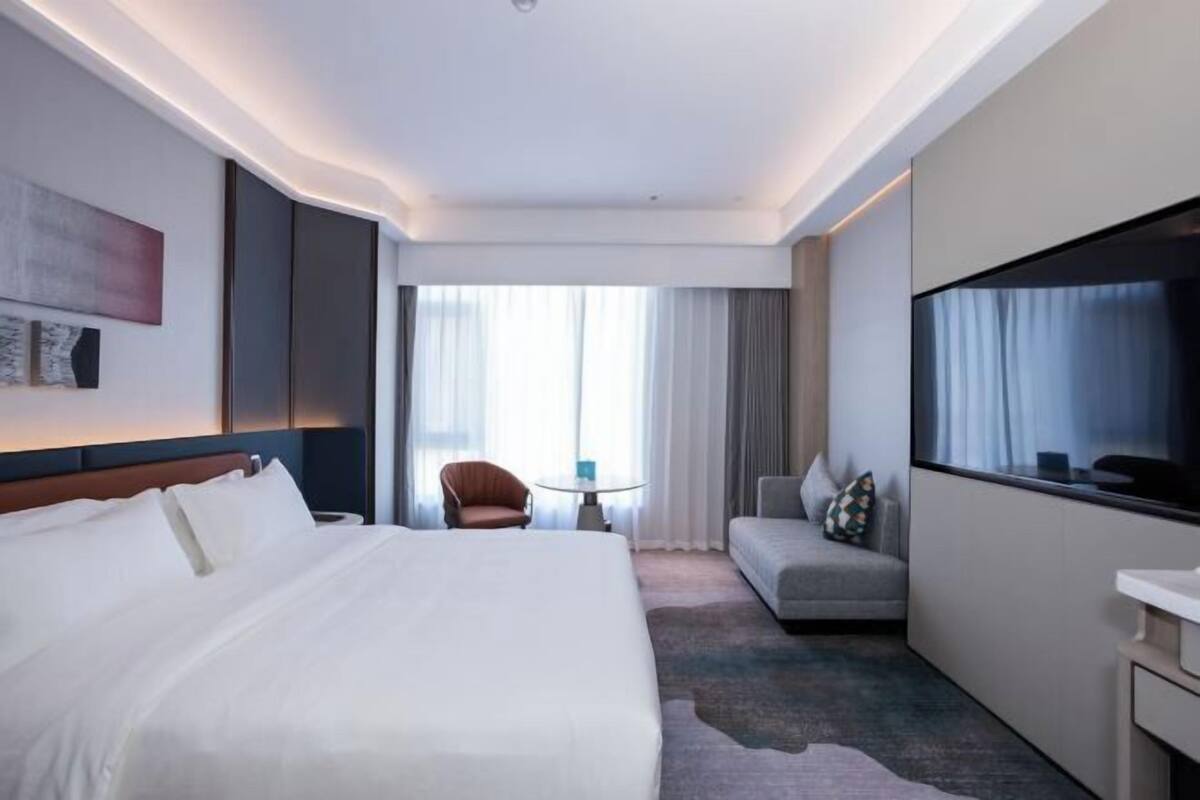 Ein Hotelzimmer mit einem großen Bett, einer Couch, einem Fernseher, einem kleinen Tisch und einem Sessel.