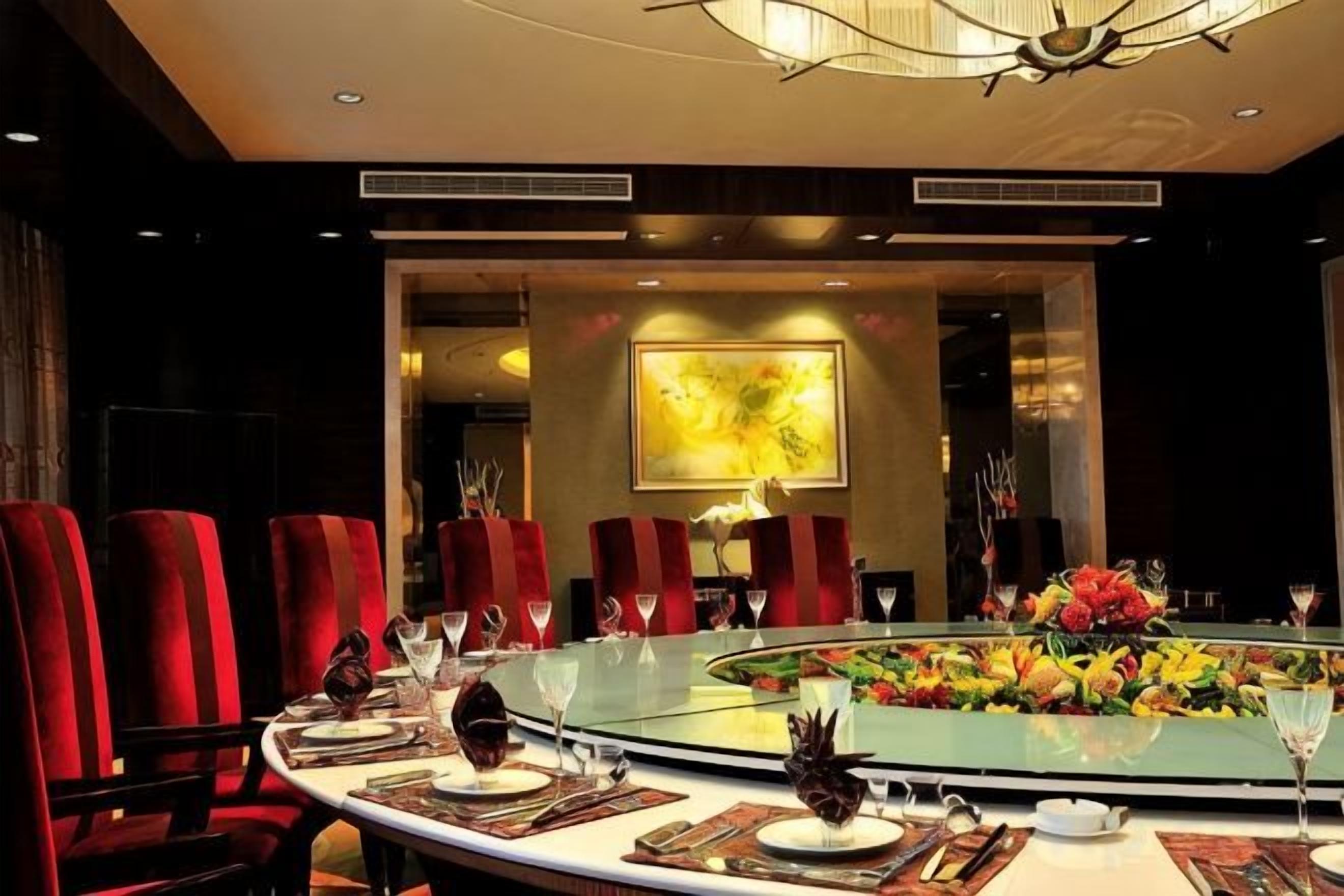 Uma sala de jantar formal com uma mesa redonda, cadeiras estofadas em vermelho e um arranjo floral central.