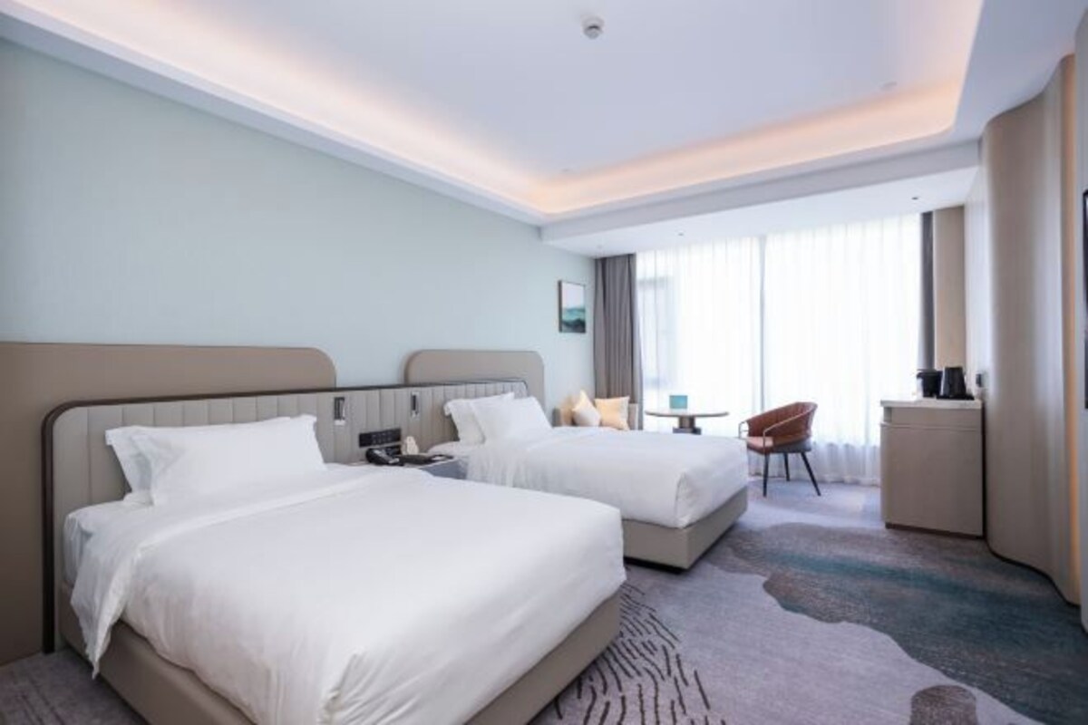 Habitación de hotel con dos camas, un escritorio, una silla y vistas a la ciudad.