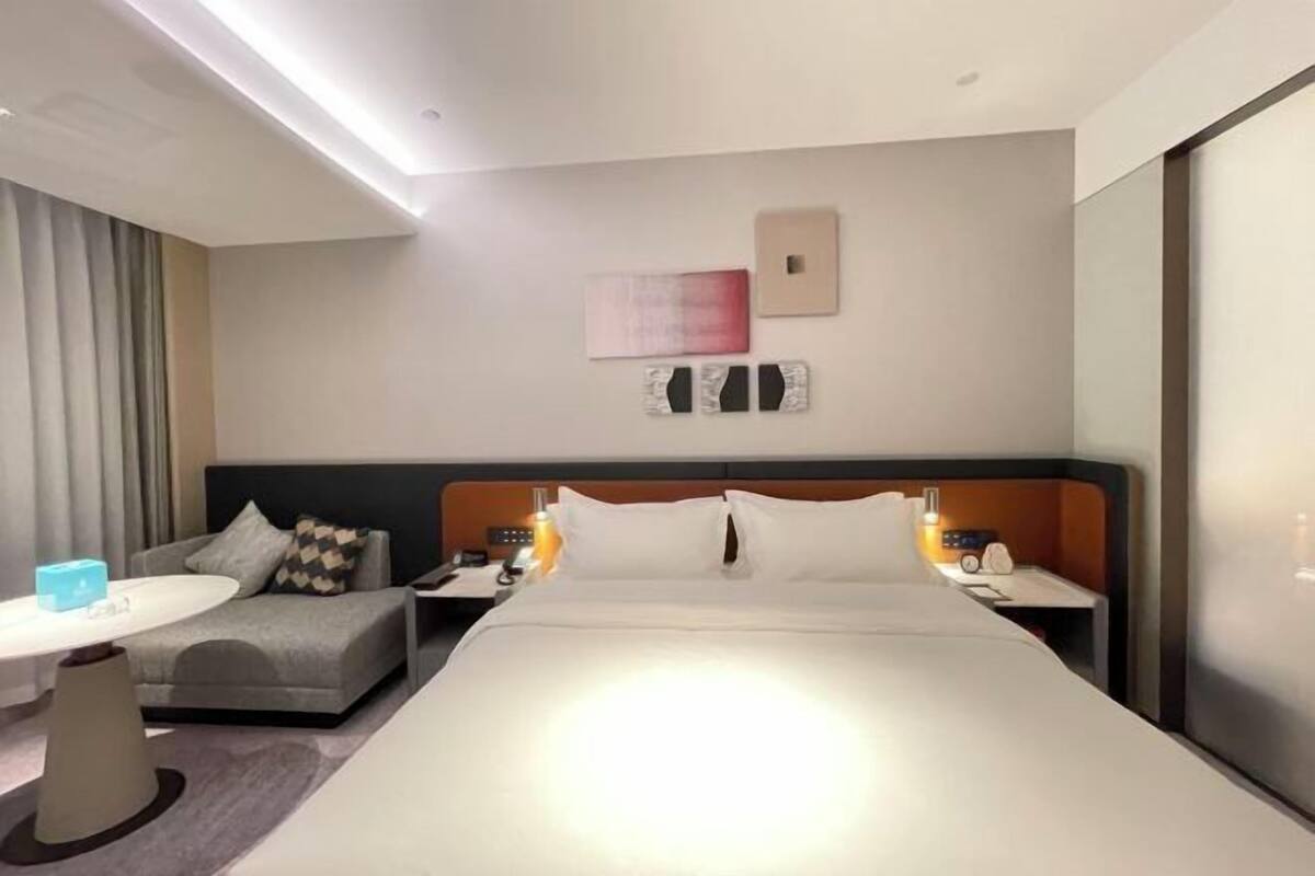 Ein modernes Hotelzimmer mit einem großen Bett, einem Nachttisch mit Lampe, einer kleinen Couch und einem Schreibtisch mit Stuhl.