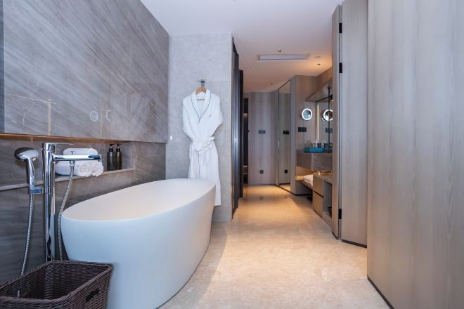 A modern bathroom with a freestanding bathtub, a robe hanging on a rack, and a mirror with lights.