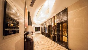 A hotel corridor with a marble floor, a reception desk, and a wall-mounted TV.