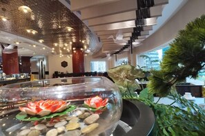 A modern lobby with a large glass fishbowl centerpiece, a staircase, and indoor plants.