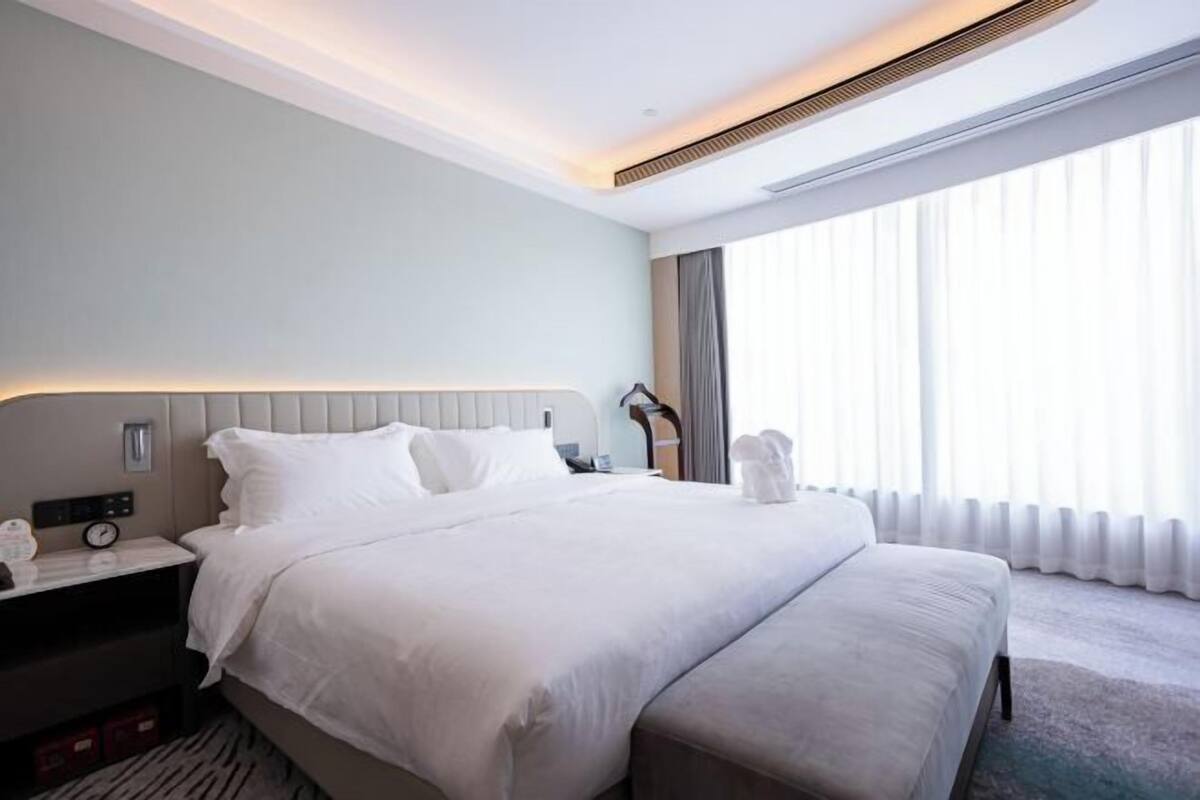 Ein modernes Hotelzimmer mit einem großen Bett, einem Nachttisch und einem Fenster mit Vorhängen.