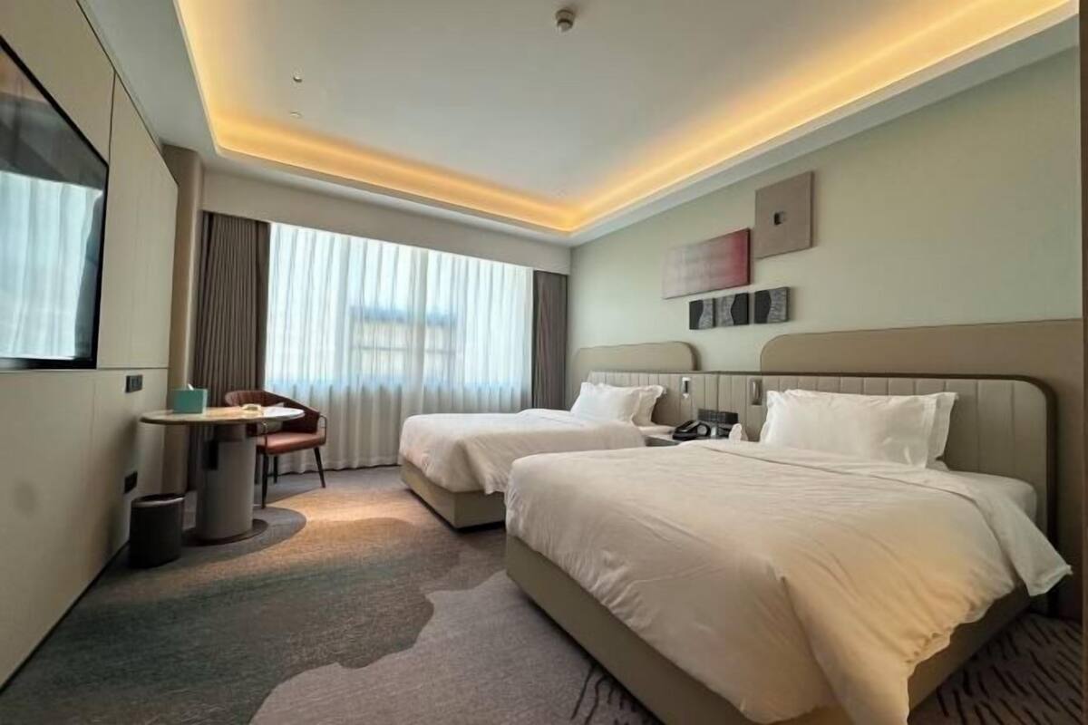 Ein Hotelzimmer mit zwei Betten, einem Schreibtisch, einem Stuhl, einem kleinen Tisch und einem Fenster mit Vorhängen.