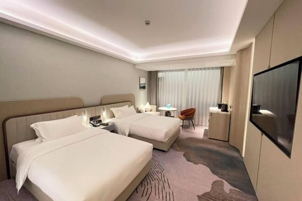 Ein Hotelzimmer mit zwei Betten, einem Schreibtisch, einem Stuhl, einem Fernseher und einem Fenster mit Vorhängen.