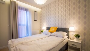 A neatly made bed with white linens, a bedside table with a lamp, and a decorative pillow with text.