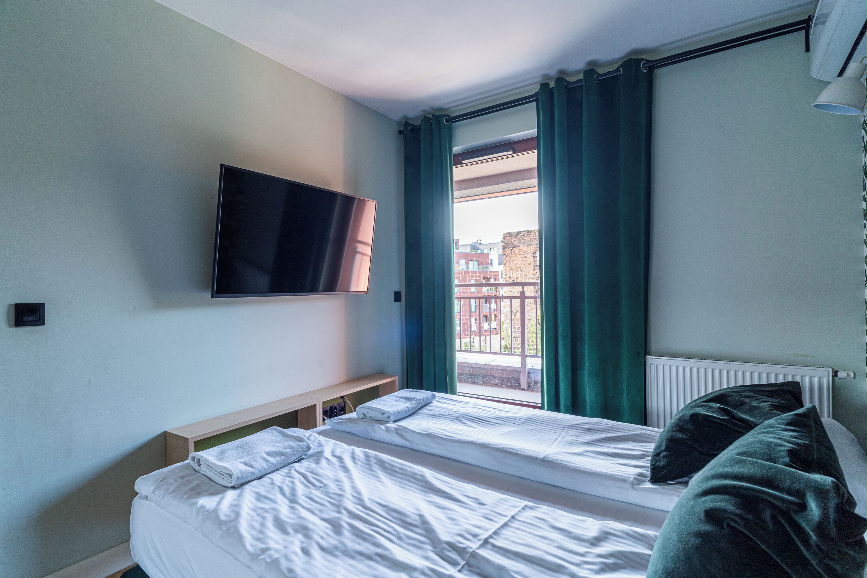 A hotel room with a bed, a TV mounted on the wall, and a window with curtains.