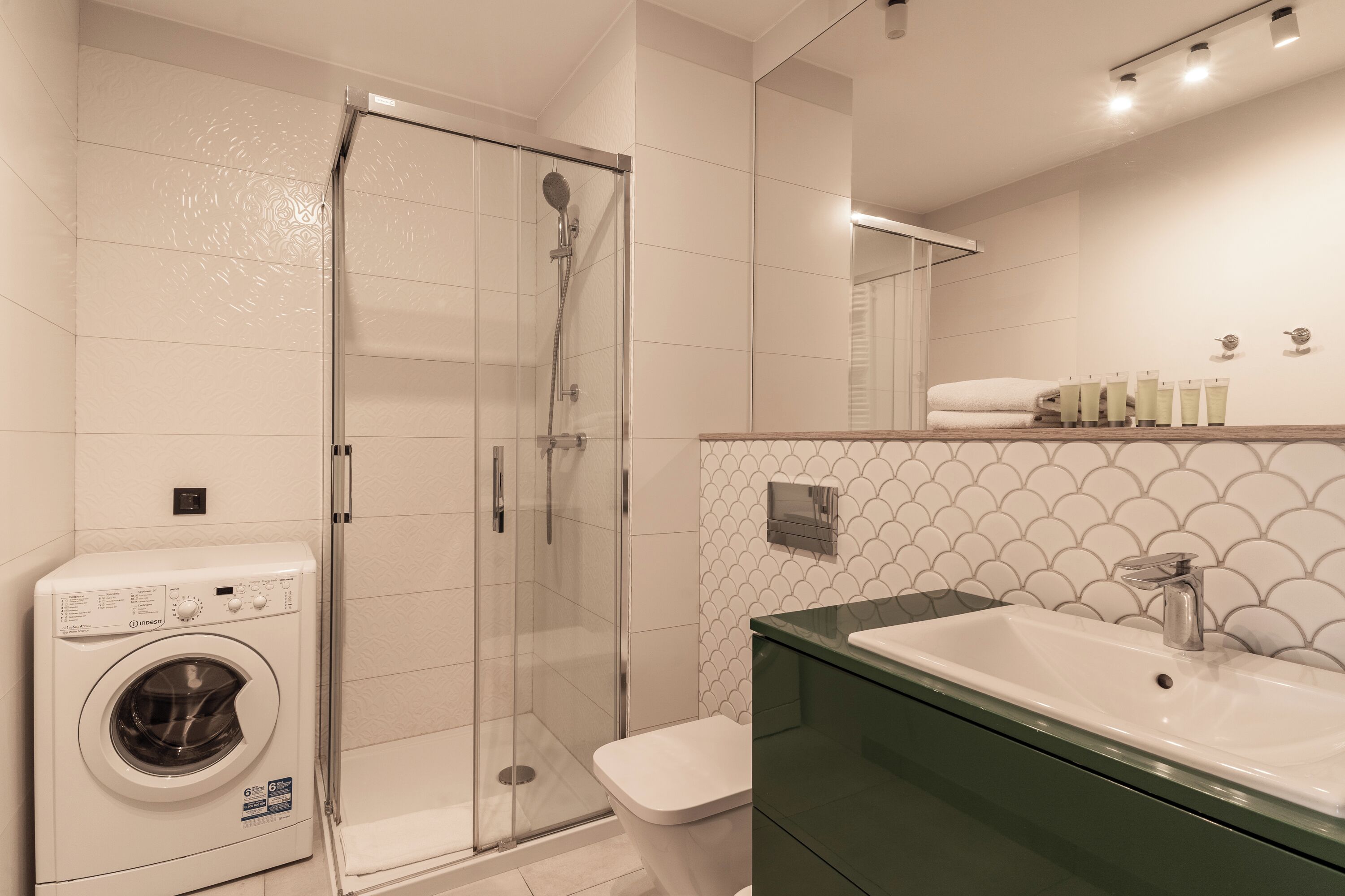 A modern bathroom with a glass-enclosed shower, a washing machine, and a sink with a green countertop.