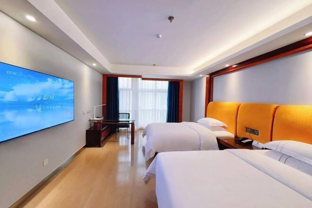 Une chambre d’hôtel avec deux lits, un téléviseur fixé au mur, un bureau et une fenêtre avec des rideaux.