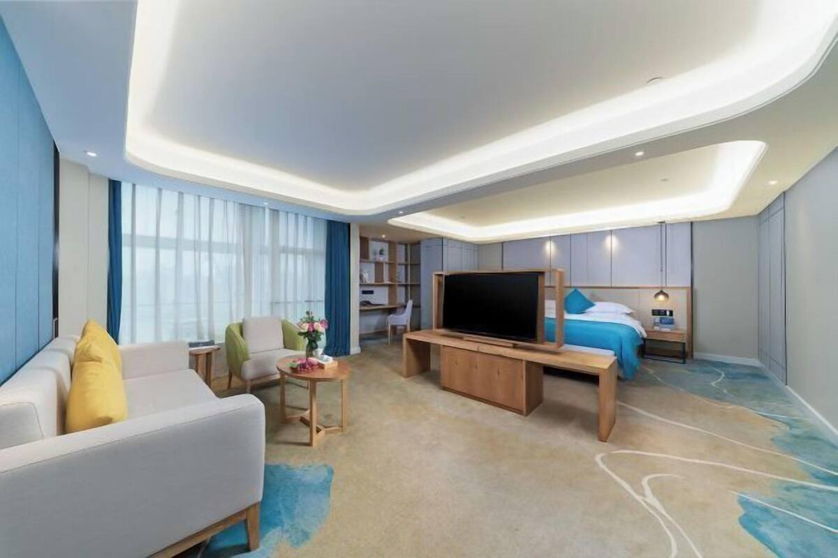 Une chambre d’hôtel moderne équipée d’un canapé, d’une télévision, d’un lit, d’un bureau et d’une petite table avec une lampe.