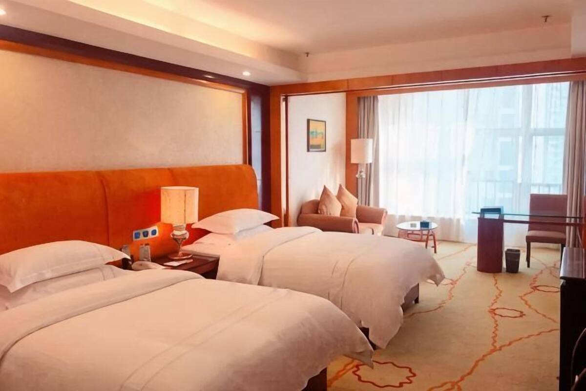 Une chambre d’hôtel avec deux lits, un bureau, une chaise, une lampe et une vue sur l’extérieur.