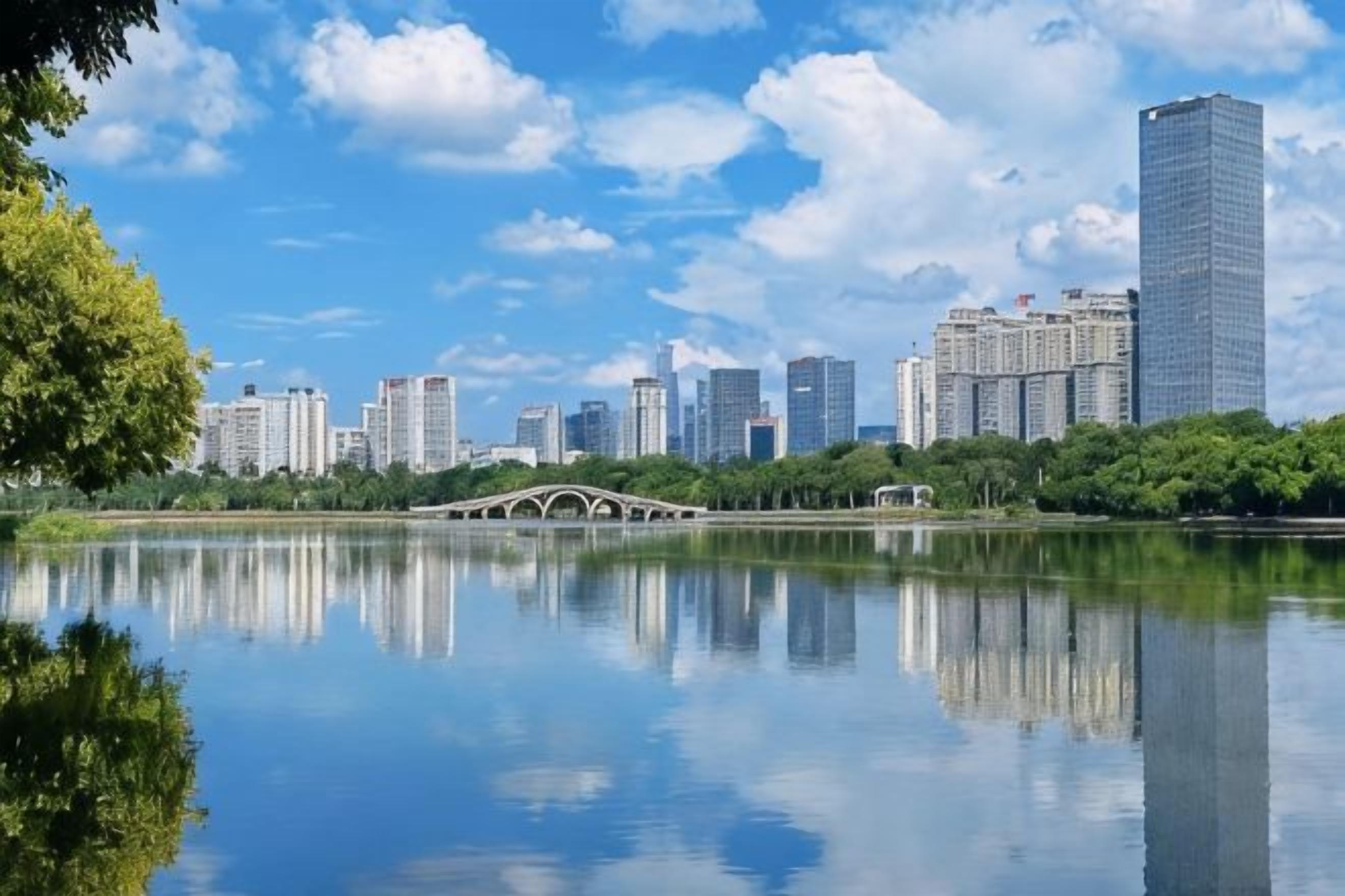 A cityscape with a bridge over a calm body of water, reflecting the buildings and sky.