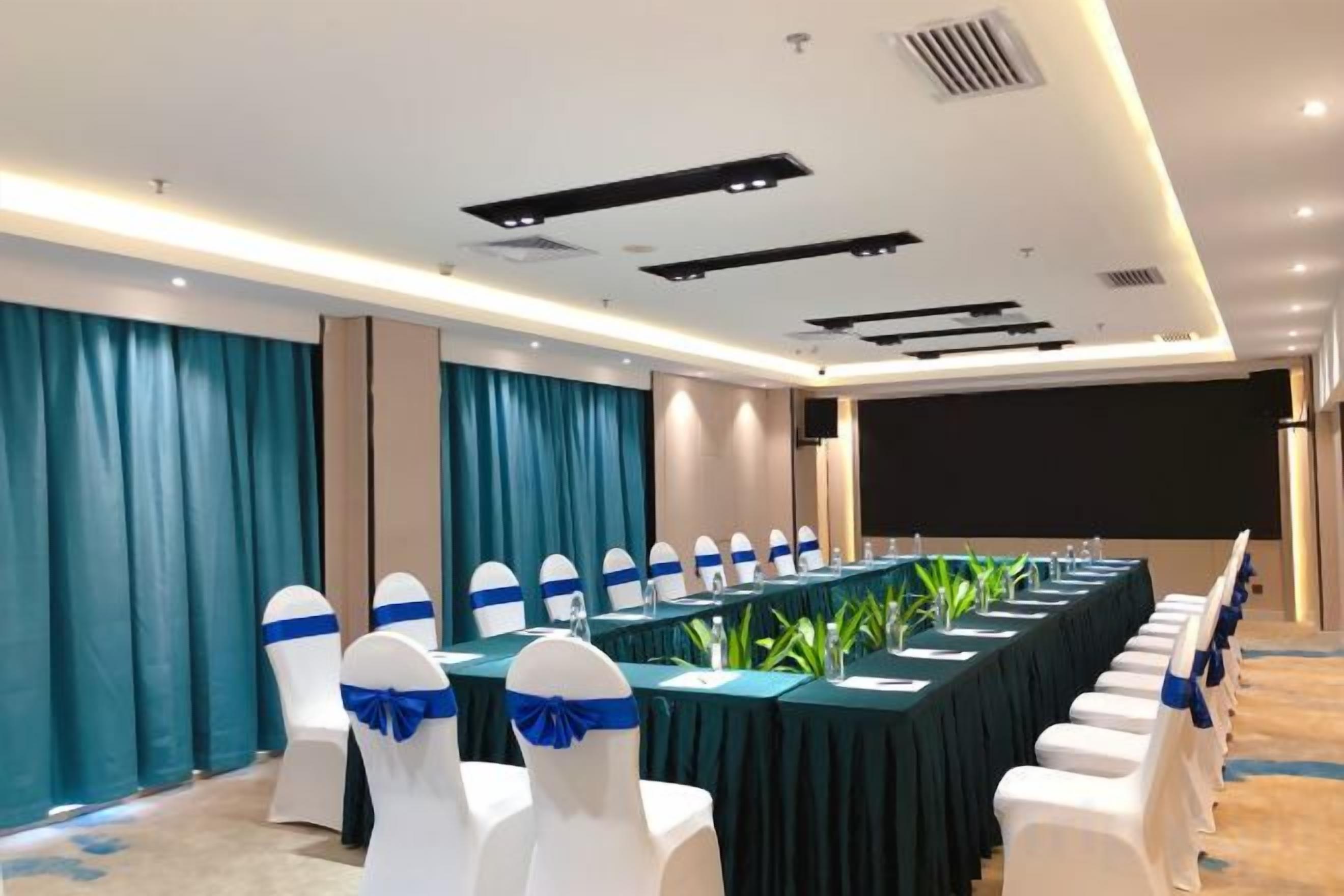 Ein Konferenzraum mit einem langen Tisch, weißen Stühlen mit blauen Bändern und einer Projektionsleinwand.