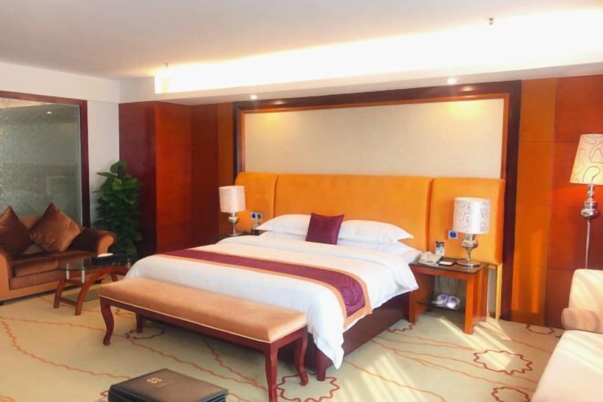 Une chambre d’hôtel avec un grand lit, un banc, une table de chevet, une lampe, une plante et un canapé.