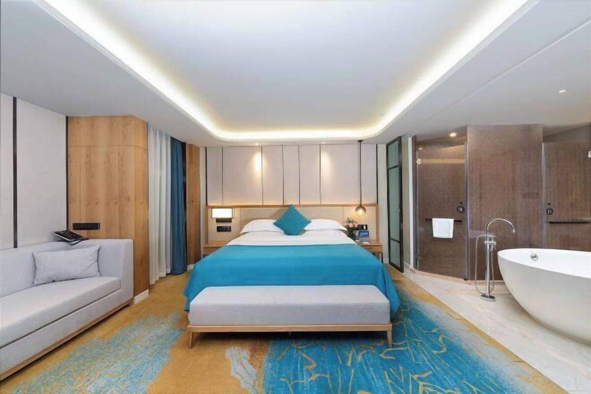 Une chambre d’hôtel moderne avec un grand lit, un canapé, une baignoire et un mur revêtu de panneaux en bois.