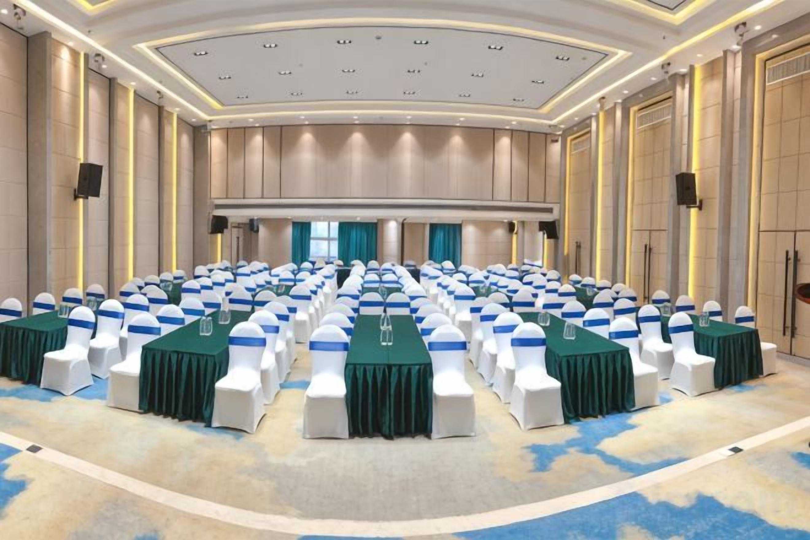 A conference room with rows of tables and chairs, a stage, and a large screen.