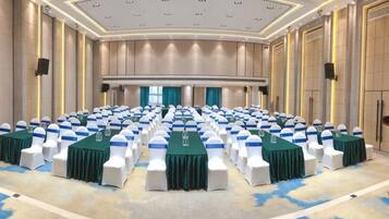 A conference room with rows of tables and chairs, a stage, and a large screen.